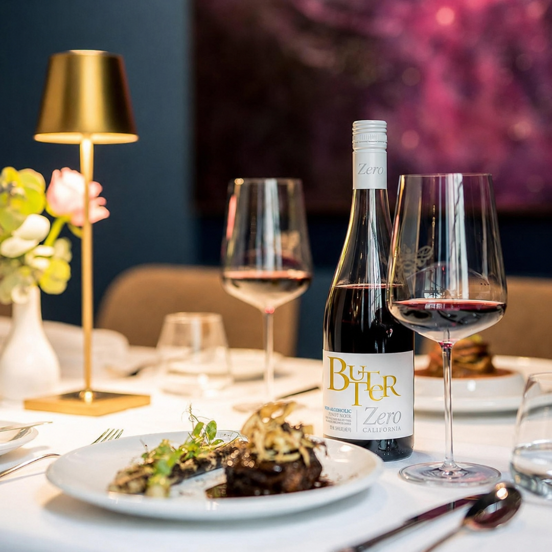 Table, two glasses with red wine, plate with lambchop, and butter zero pino noir