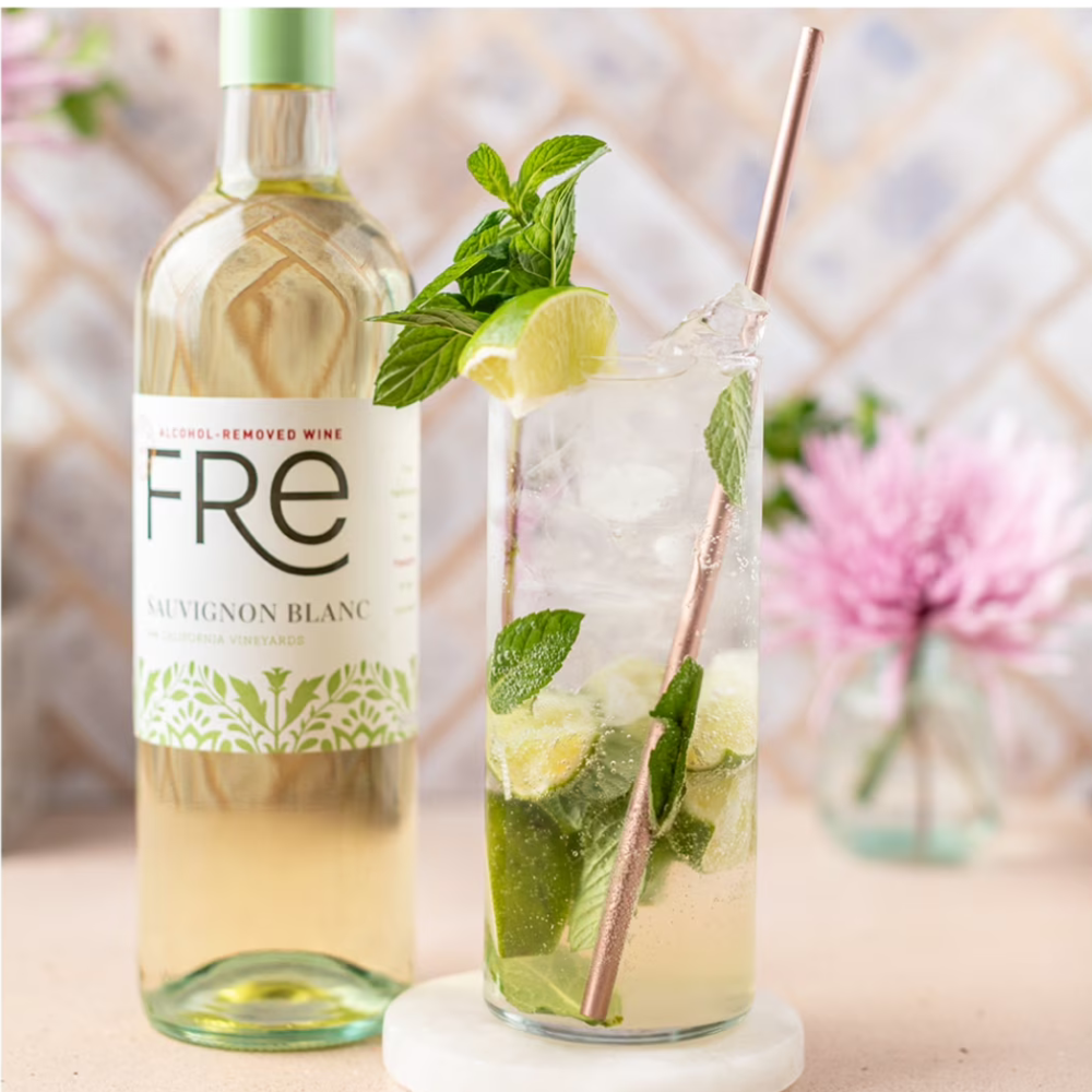 Bottle of Fre Sauvignon Blanc with a glass of lemonade and mint leaves on a blurred outdoor background.