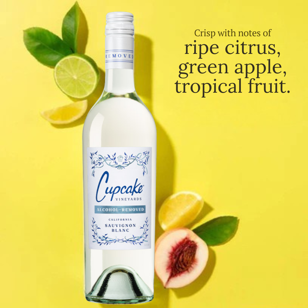 A bottle of Cupcake Vineyards California Sauvignon Blanc alcohol-free wine on a bright yellow background, styled with citrus, green apple slices, and a peach. Text on the right reads: 'Crisp with notes of ripe citrus, green apple, tropical fruit.