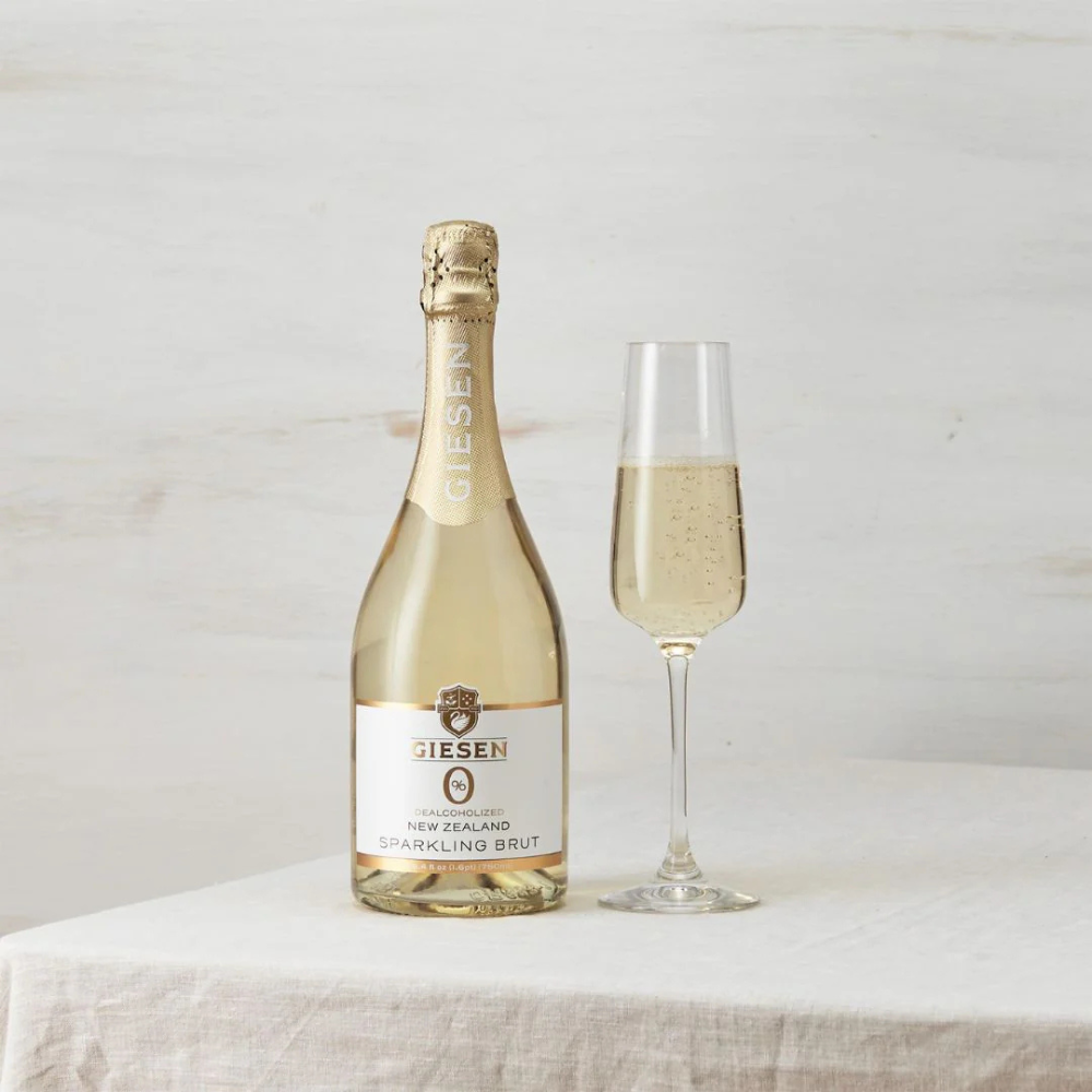 Bottle and glass of Dienes sparkling wine on a white surface with a light background