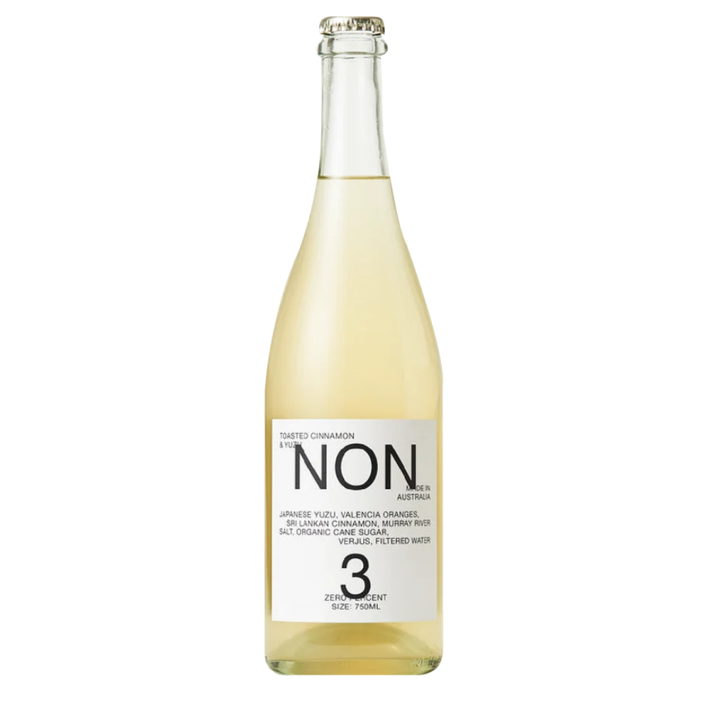 A bottle of Non 3% Non-Alcoholic Sparkling Cinnamon Orange juice, featuring a clear glass bottle filled with pale golden liquid and a white label with black text, set against a plain white background.