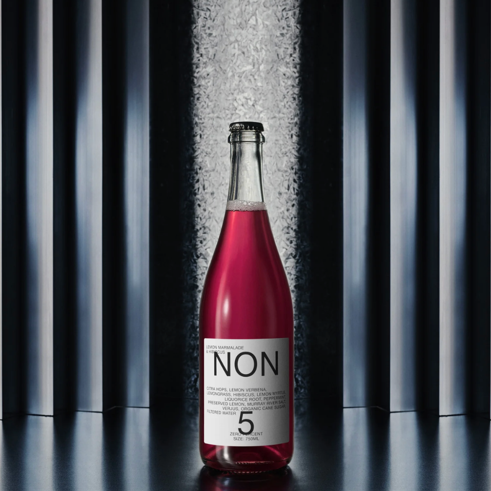A clear glass bottle of NON 5 sparkling wine with vibrant pink-red liquid, featuring a white label with black text, set against a dark background with vertical light streaks.